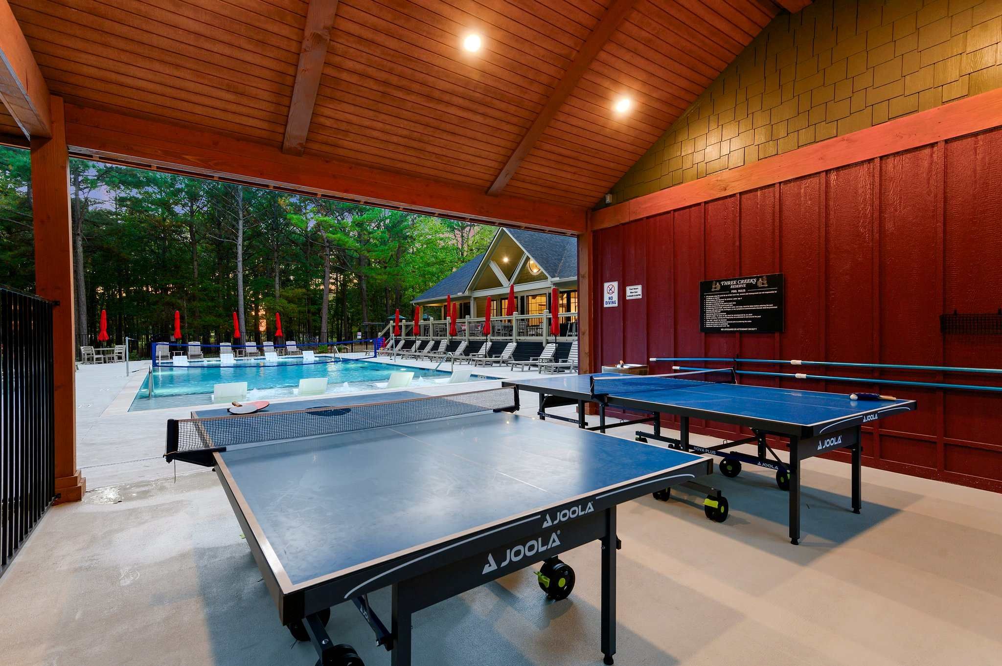 2 pingpong tables outdoor in front of a swimming pool.